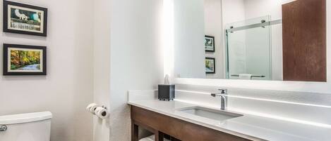 A modern bathroom with a white sink, a large mirror, and framed pictures on the wall.