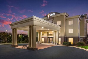 Un hotel con entrada techada, un letrero de Comfort Inn & Suites y fachada de ladrillo.