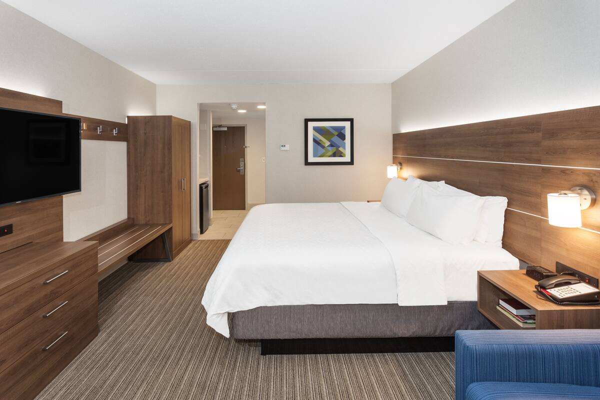 A hotel room with a large bed, a TV, a desk with a lamp, and a framed picture on the wall.