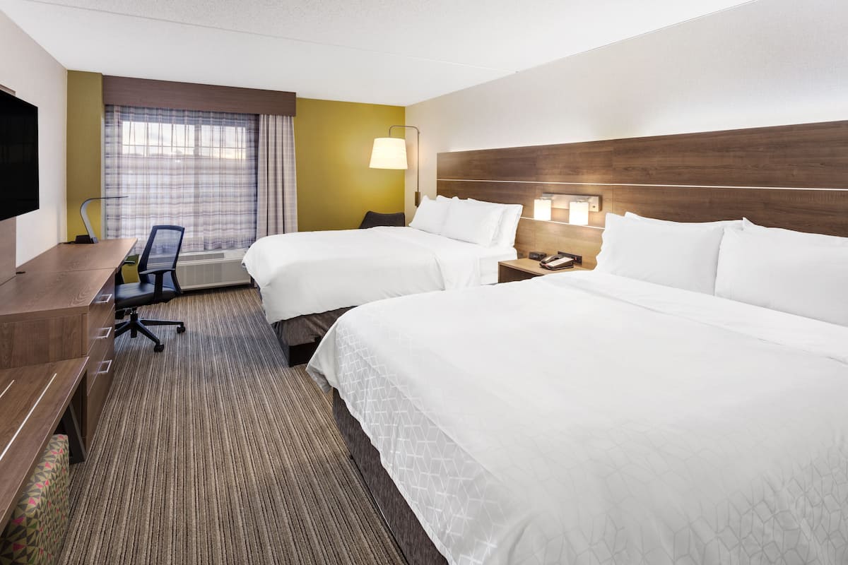 A hotel room with two beds, a desk, a chair, a TV, and a window with curtains.