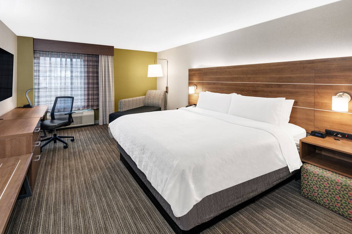 A hotel room with a large bed, a desk with a chair, a TV, and a window with curtains.