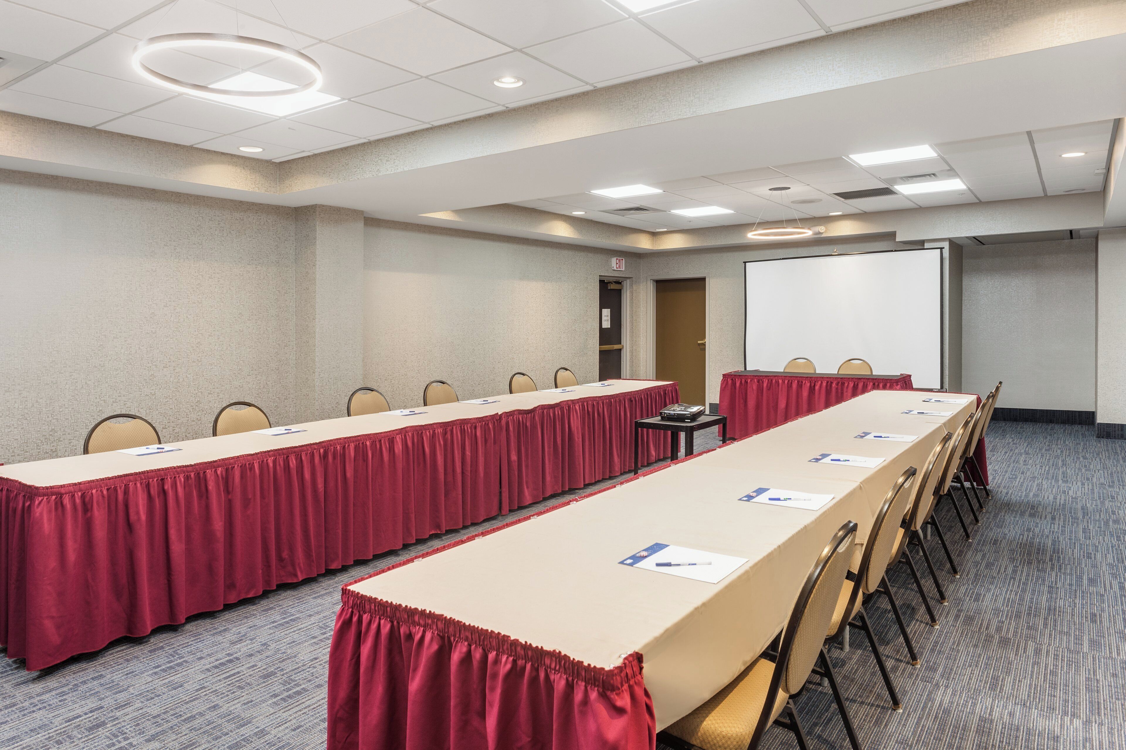 Un salón de conferencias con una larga mesa, sillas, una pantalla de proyector y una puerta de salida.