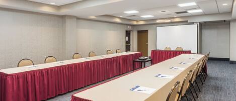 A conference room with a long table, chairs, a projector screen, and an exit door.