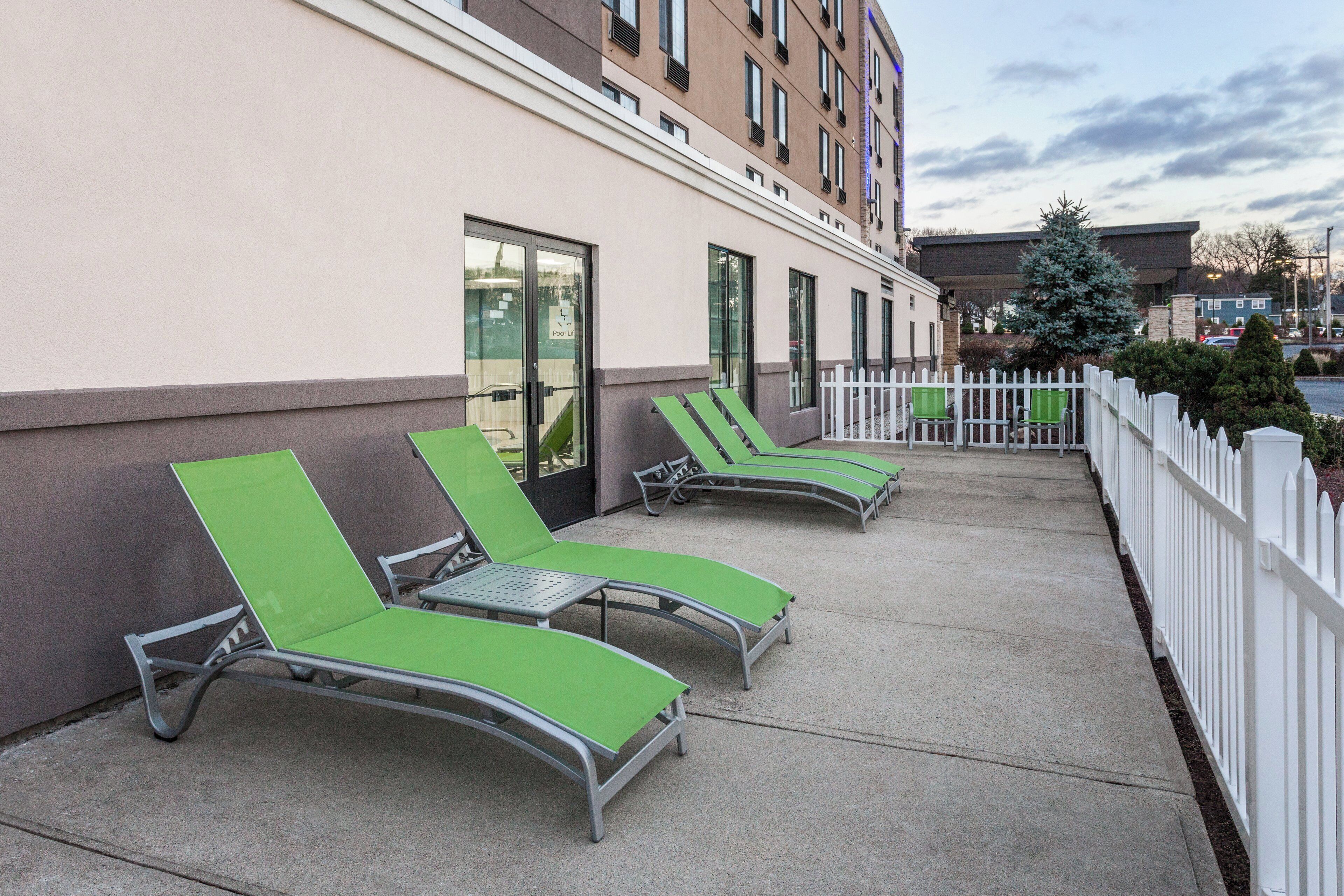 Un bâtiment avec un panneau indiquant la présence d’un ascenseur pour la piscine, des chaises longues à l’extérieur et une clôture blanche en bois.