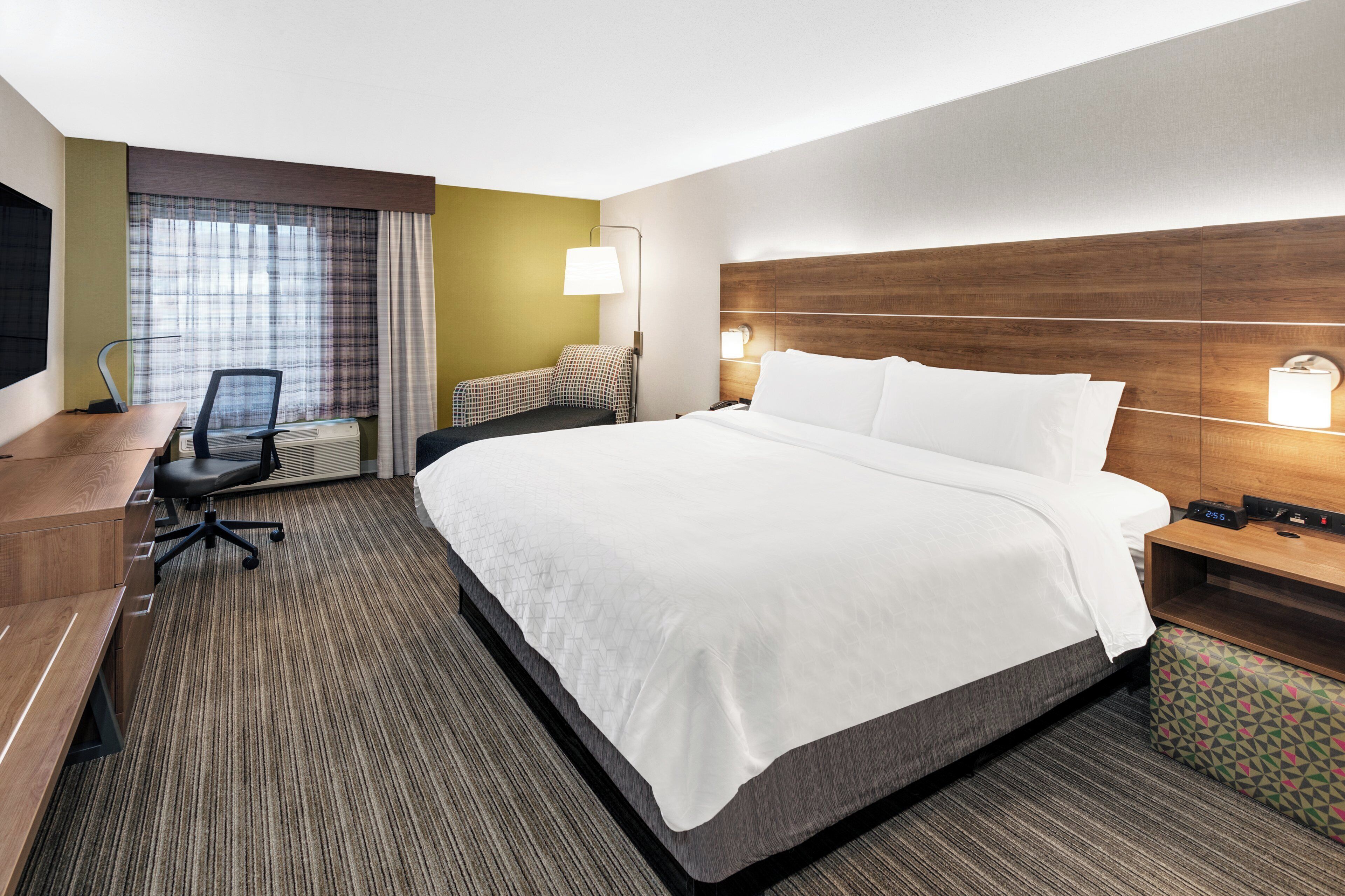 A hotel room with a large bed, a desk with a chair, a TV, and a window with curtains.