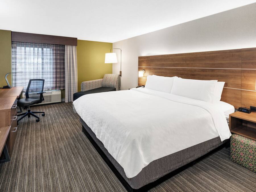 A hotel room with a large bed, a desk with a chair, a TV, and a window with curtains.