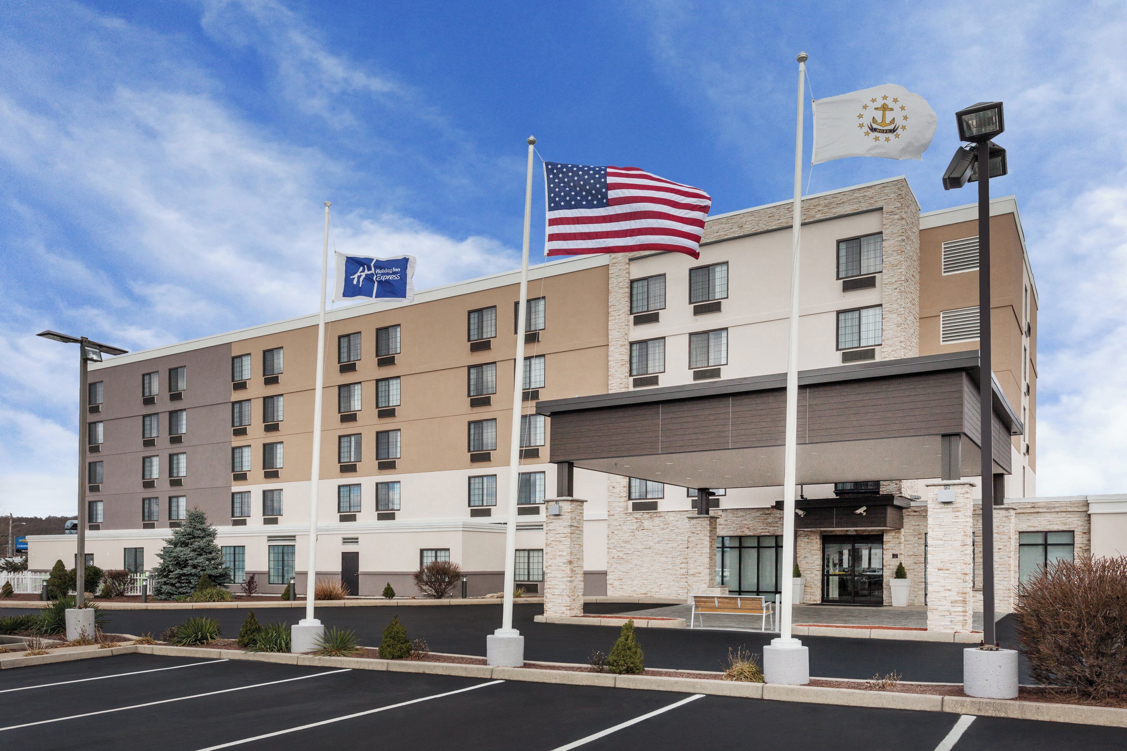 A multi-story hotel with a parking lot in front, featuring a flagpole with the American flag and a Holiday Inn Express sign.