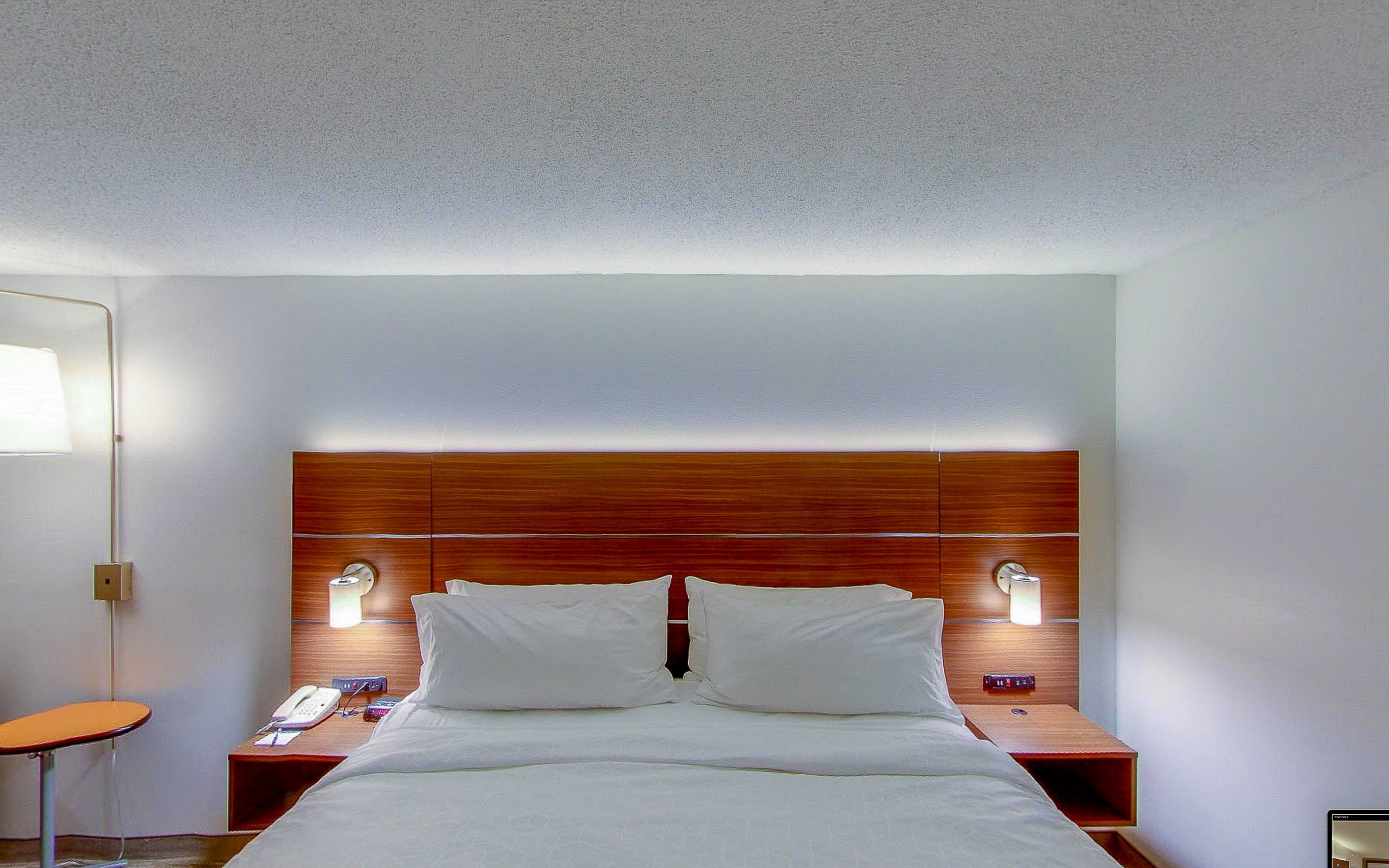 A hotel room with a wooden headboard, two bedside lamps, a telephone, and a small table.