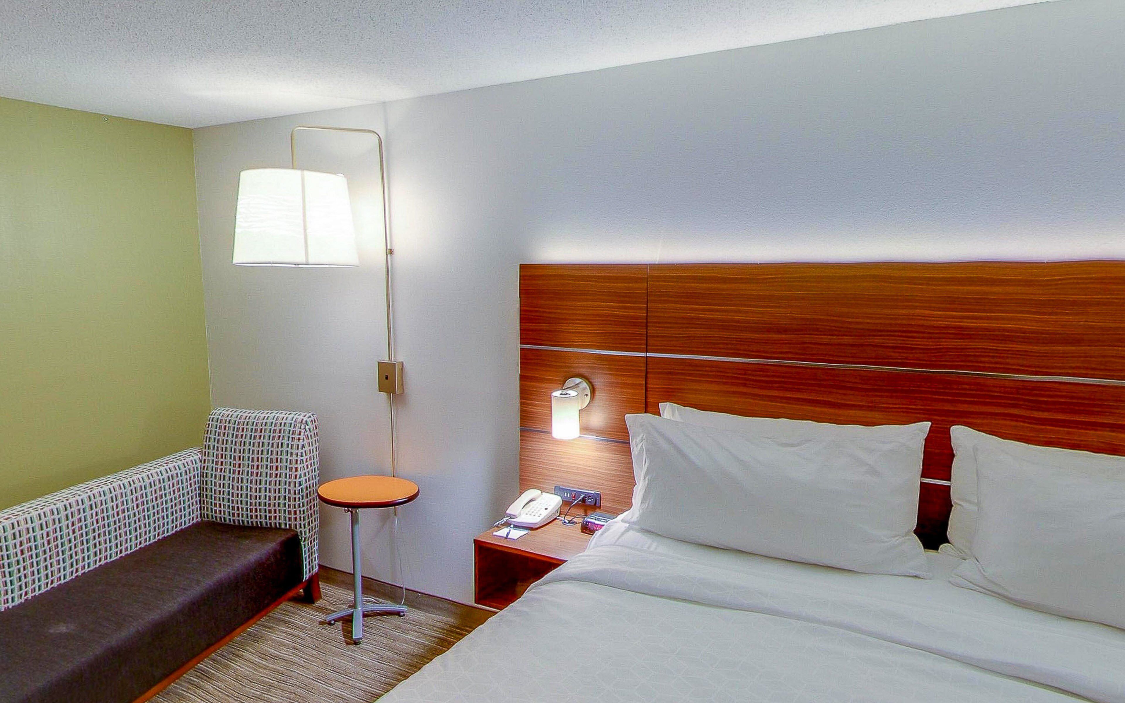 A hotel room with a bed, bedside table, lamp, and a small round table.
