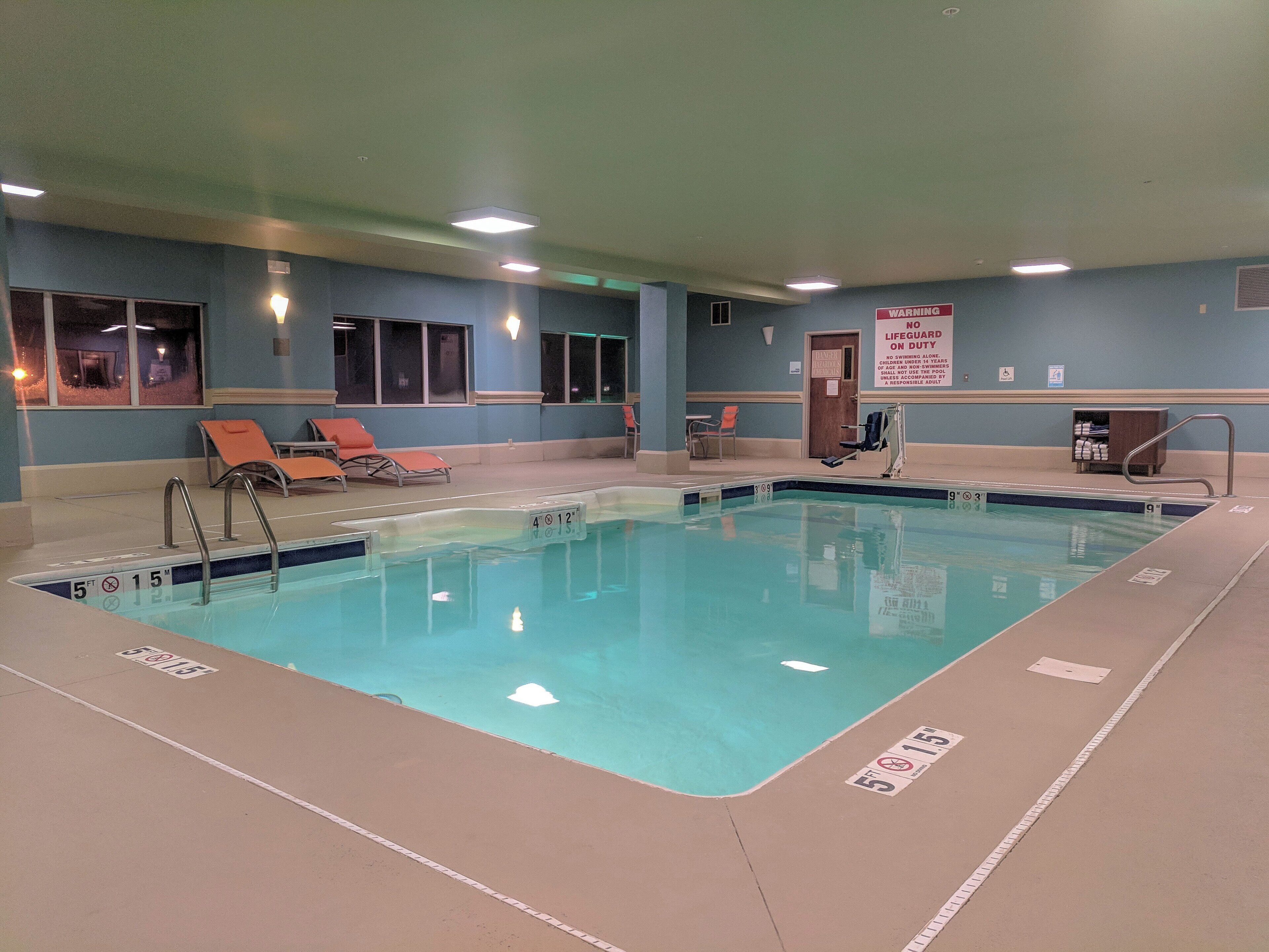 An indoor swimming pool with clear lane markings, lounge chairs, and a lifeguard station.