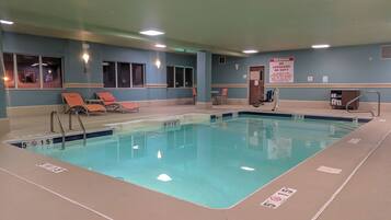 An indoor swimming pool with clear lane markings, lounge chairs, and a lifeguard station.