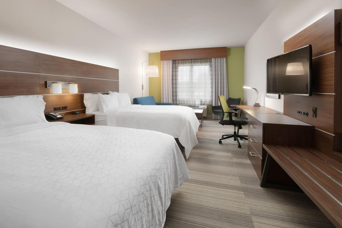 A hotel room with two beds, a desk, a chair, a TV, and a window with curtains.