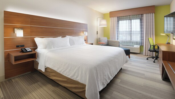 Une chambre d’hôtel avec un grand lit, un bureau, une chaise et une fenêtre avec des rideaux.