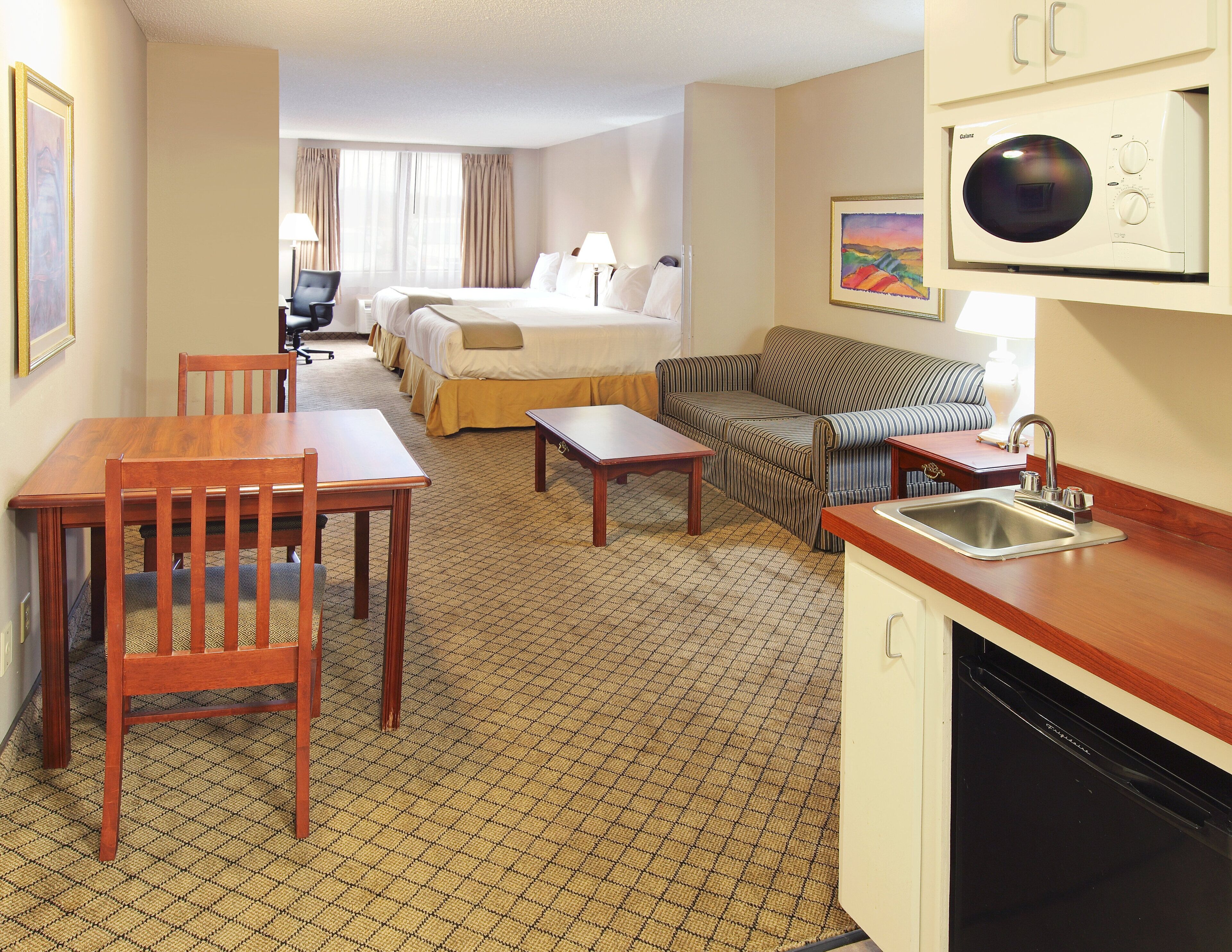 Habitación de hotel con cama, sofá, mesa de comedor y cocina equipada con lavaplatos y microondas.