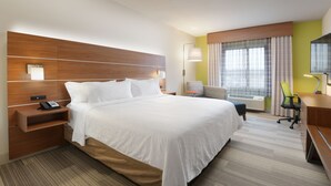 Une chambre d’hôtel avec un grand lit, un bureau, une chaise, une lampe et une fenêtre avec des rideaux.