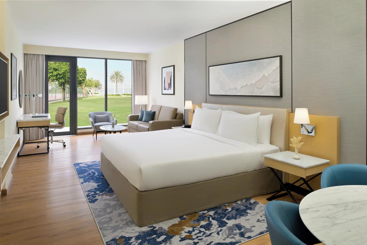 Ein Hotelzimmer mit einem großen Bett, einem Schreibtisch mit Stuhl, einem kleinen runden Tisch und Blick ins Freie.