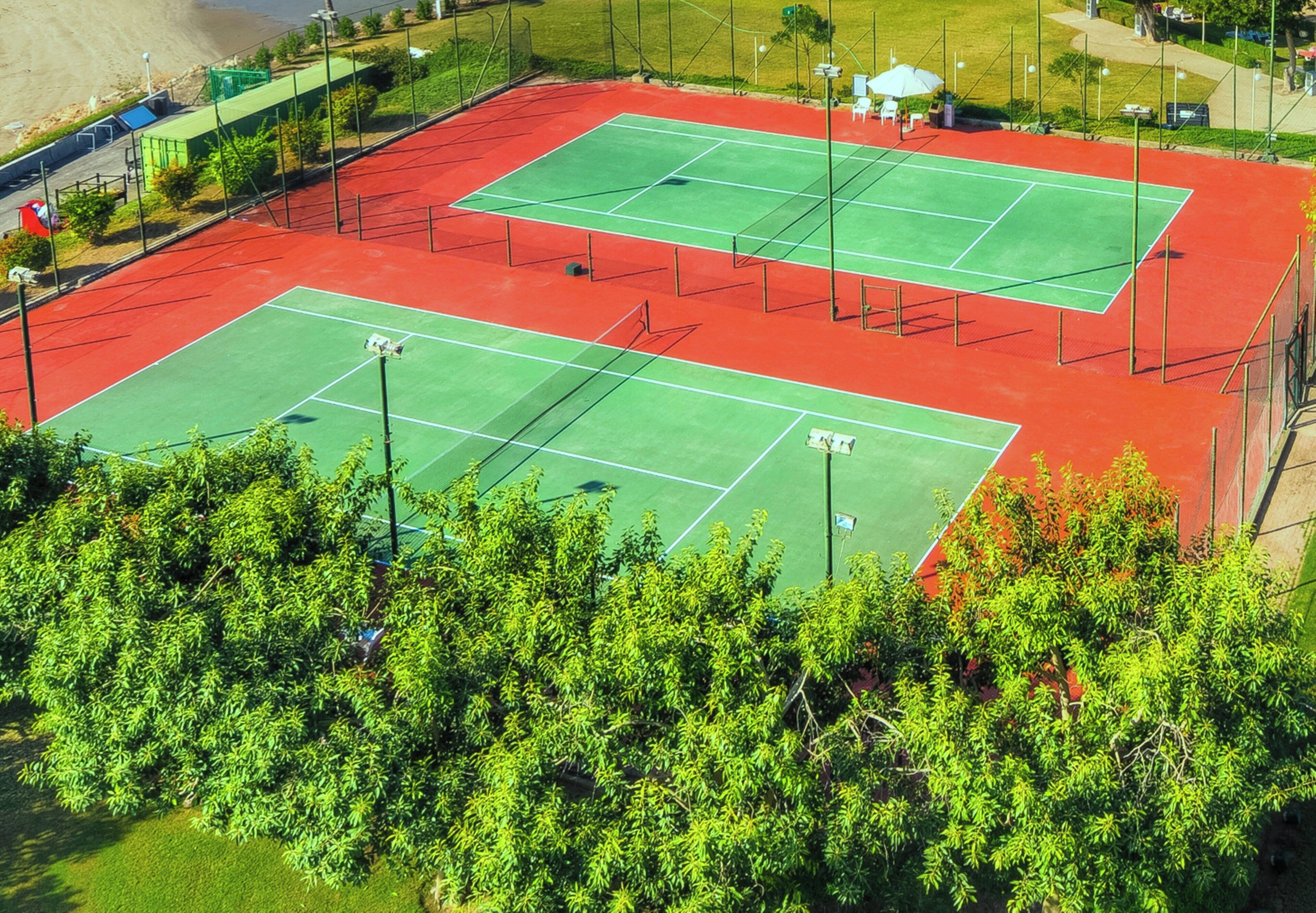 Vista aerea di un complesso di campi da tennis, con più campi circondati da alberi e un prato verde.