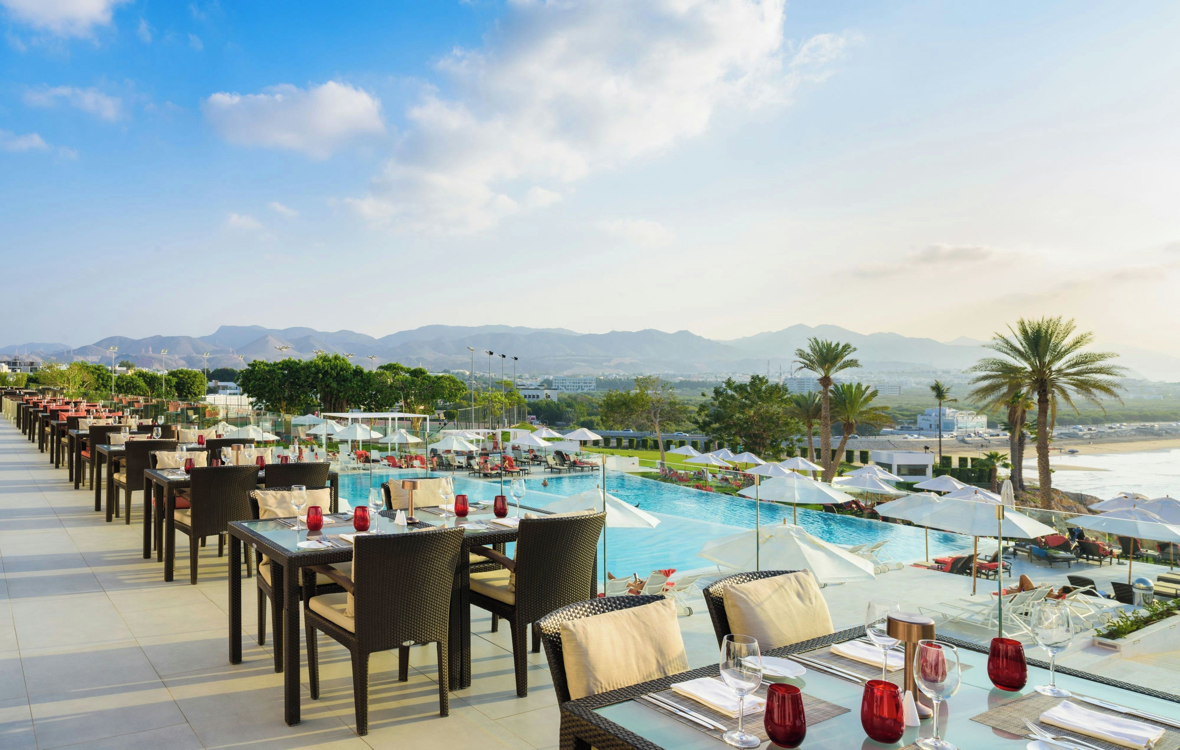 Un área de comedor en la azotea con mesas y sillas con vista a una piscina y una playa.