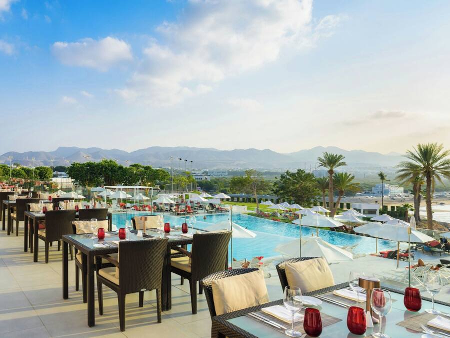 Un área de comedor en la azotea con mesas y sillas con vista a una piscina y una playa.