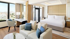 A hotel room with a bed, a sofa, a desk, and a view of the city.