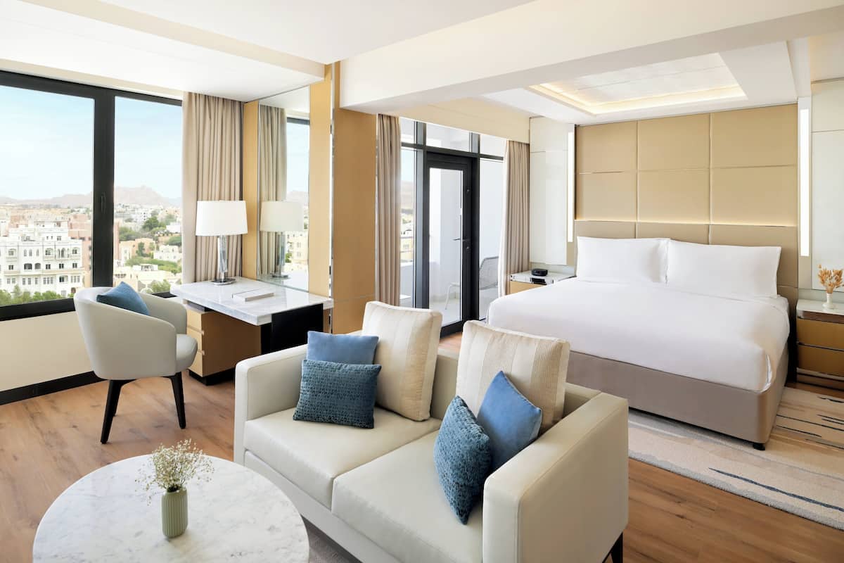 A hotel room with a bed, a sofa, a desk, and a view of the city.