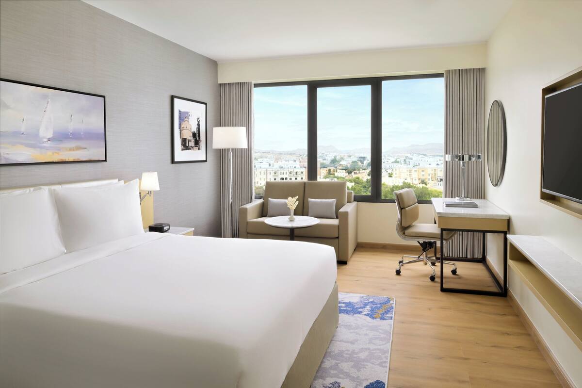A hotel room with a large bed, a sofa, a desk, and a view of the city.