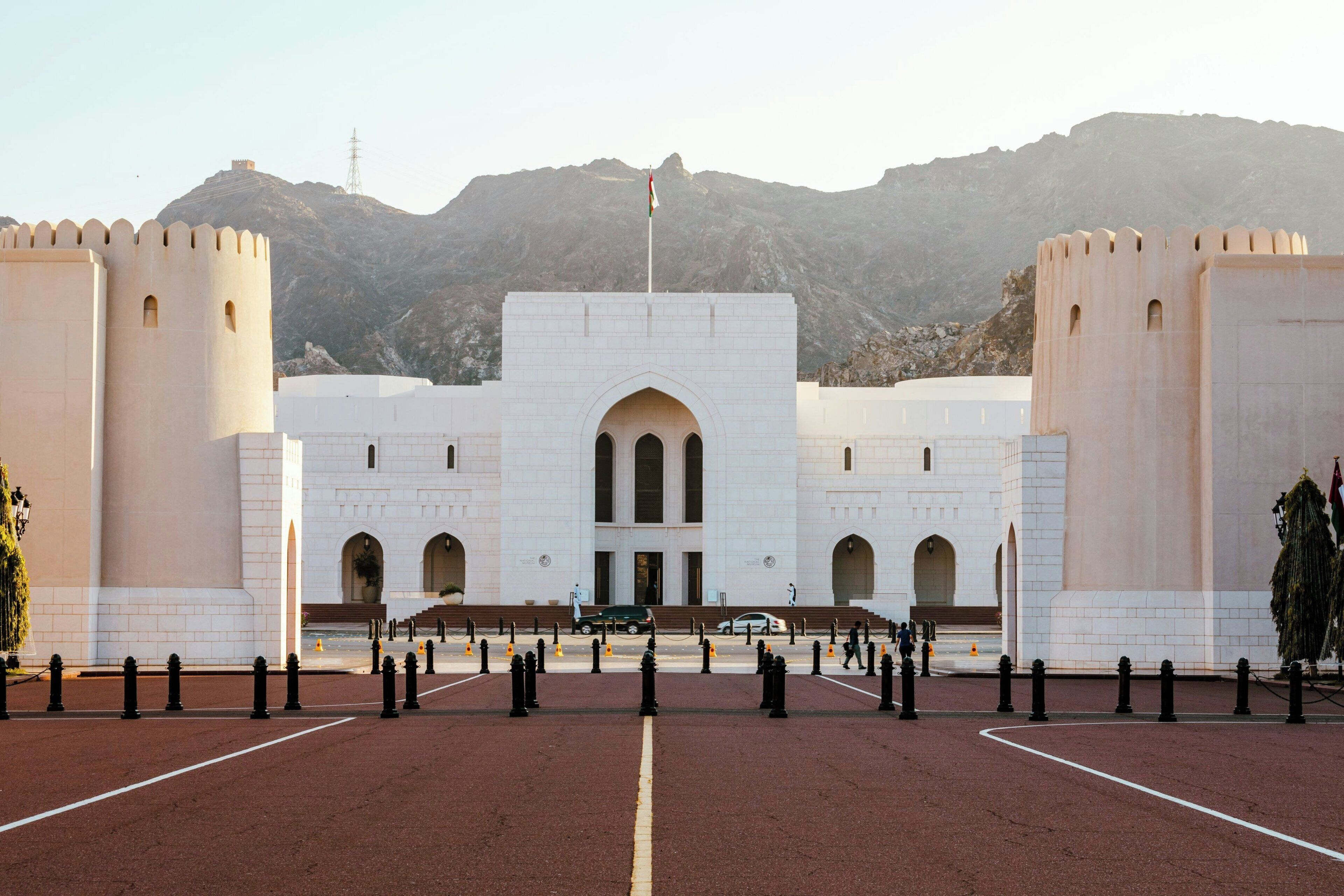 A large, fortress-like building with a central arched entrance, flanked by two tall towers, set against a mountainous backdrop.