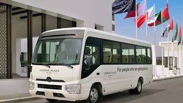 A white bus with "CROWNE PLAZA BY IHG" branding parked in front of a building with multiple flags.