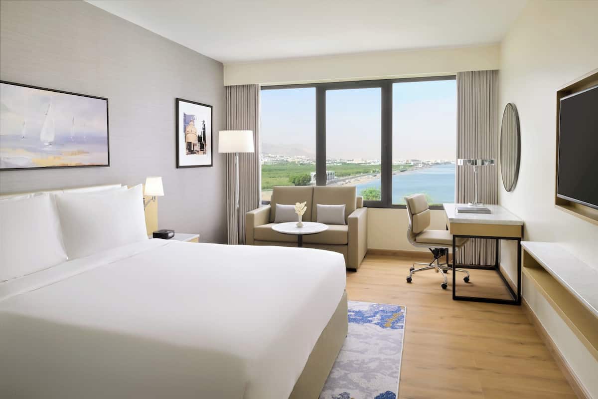 A hotel room with a large bed, a desk, a sofa, and a view of the sea.