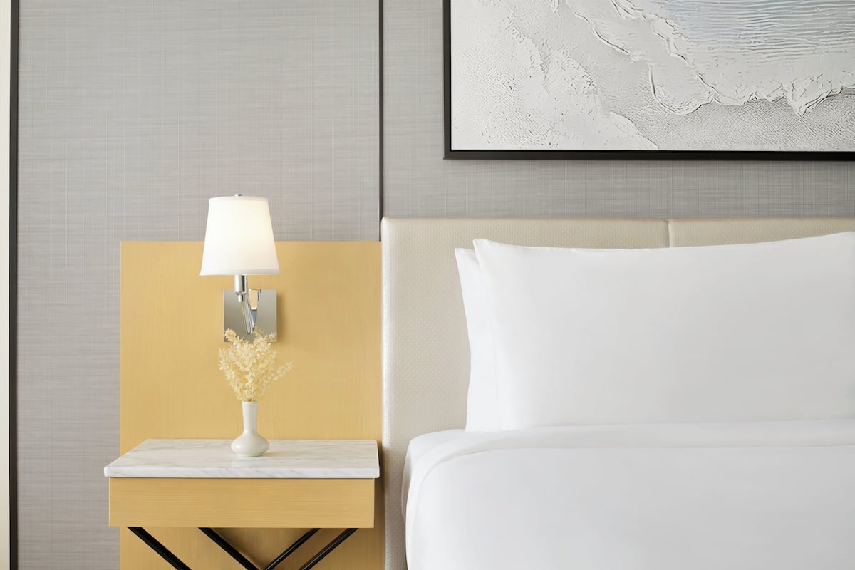 A hotel room with a bed, a nightstand with a lamp, and a wall-mounted artwork.