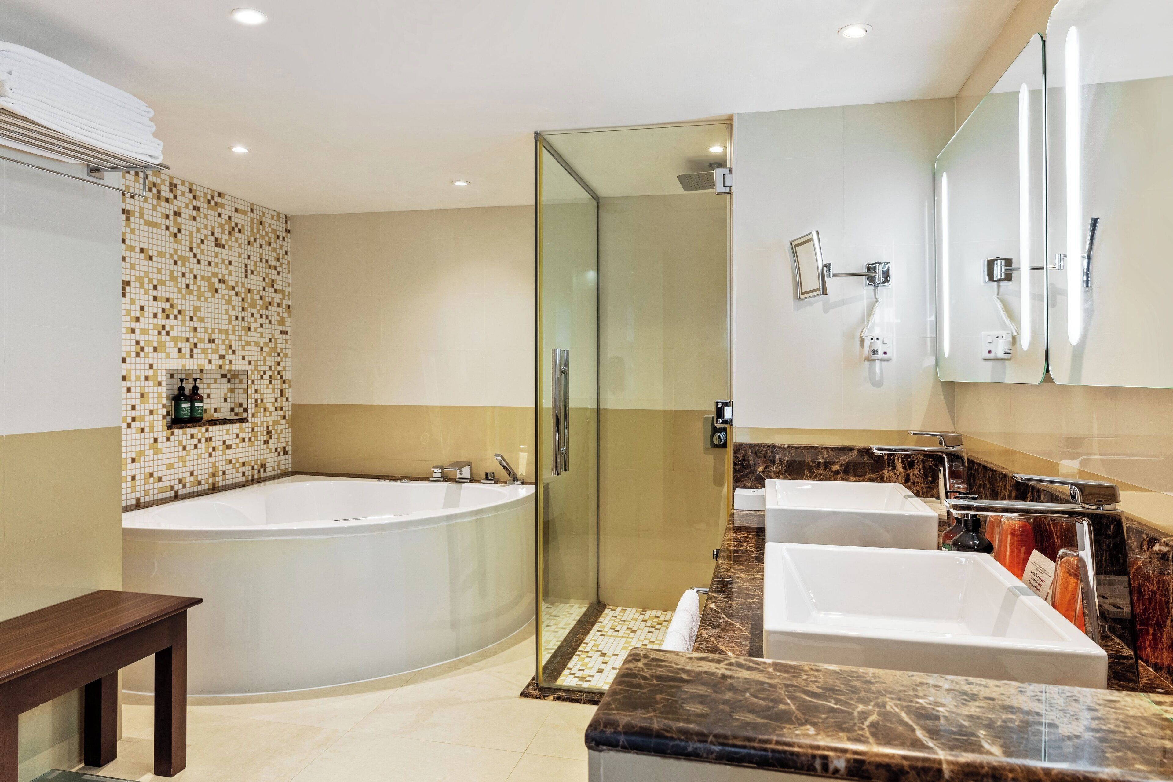 A modern bathroom with a large bathtub, a glass-enclosed shower, and two sinks.