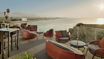 Une terrasse dotée de meubles en osier, d’une table et offrant une vue sur la mer et les montagnes.