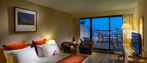 A hotel room with a large bed, a desk with a computer, a chair, and a view of the city at night.