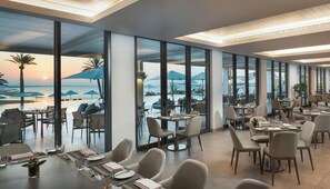 A restaurant with a view of the beach and ocean, featuring tables and chairs arranged for dining. - Crowne Plaza Muscat by IHG (Muscat)
