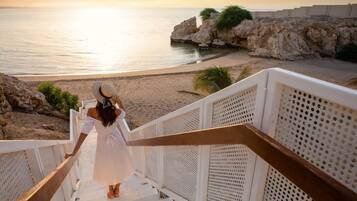 Una persona baja por una escalera metálica blanca con vistas a una playa y un litoral rocoso.