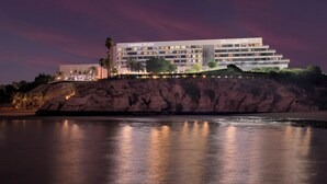 A hotel with a modern design, located on a cliff overlooking a body of water.
