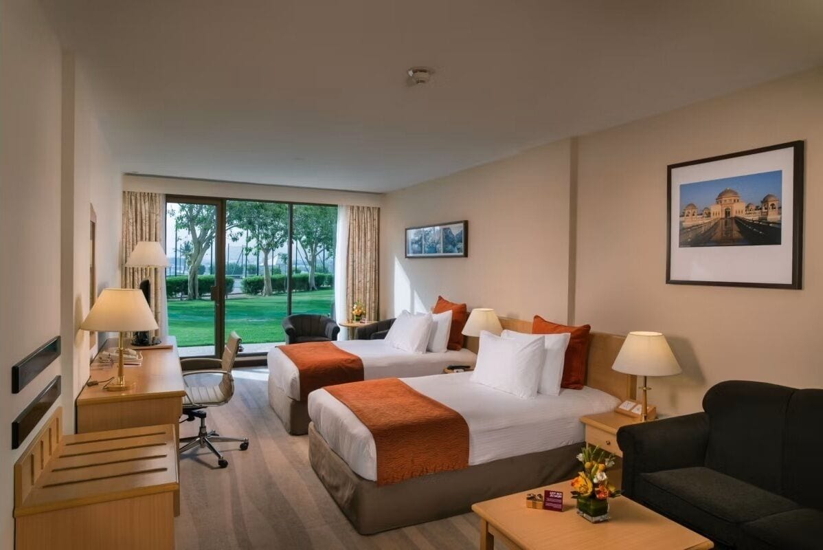 Une chambre d’hôtel avec deux lits, un bureau, une chaise, un canapé et une vue sur un jardin.