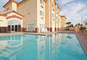 Una piscina con sillas de descanso y un edificio con varias ventanas y balcones.