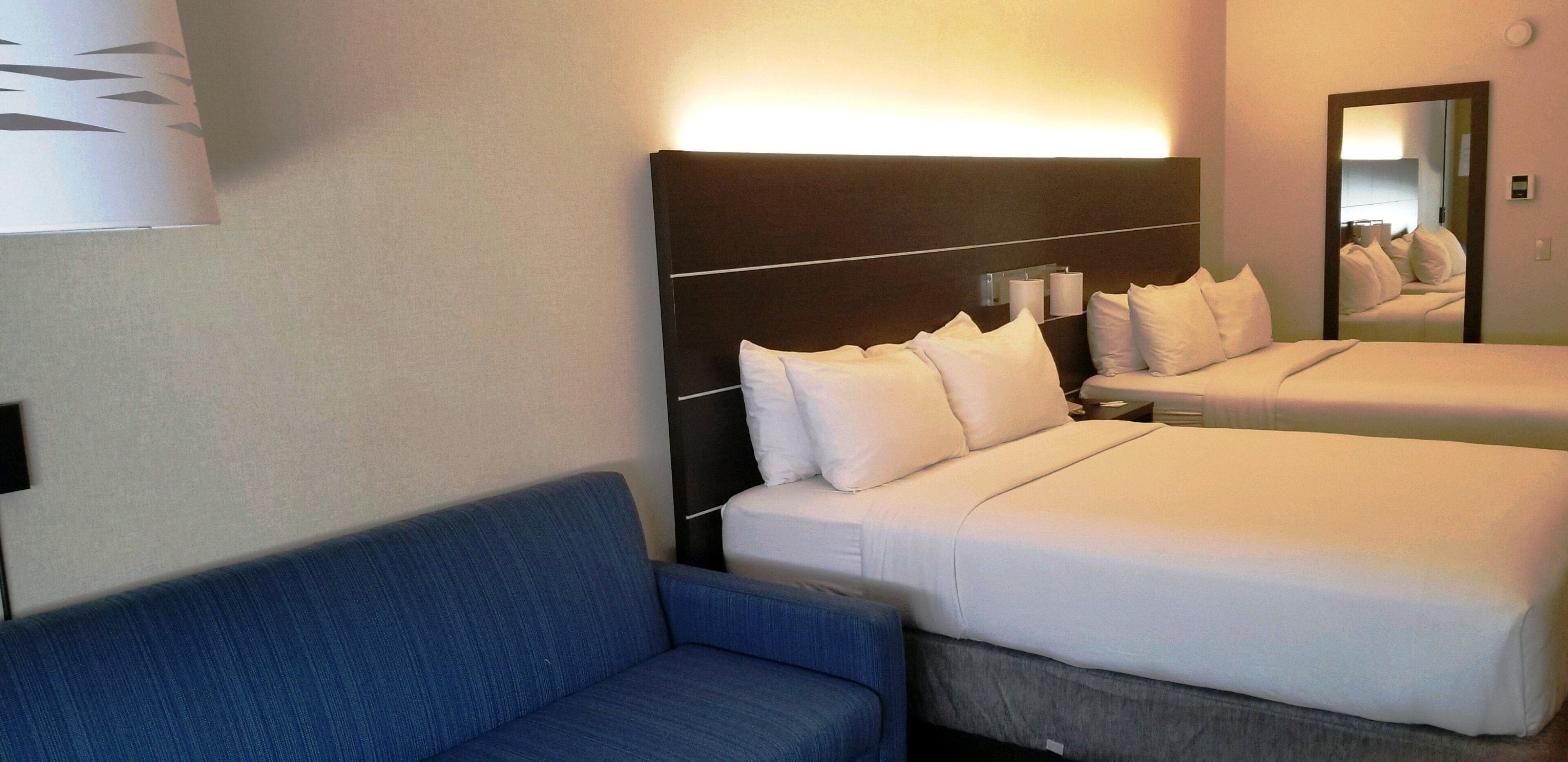 Habitació d'hotel amb dos llits, un sofà blau i un mirall gran.