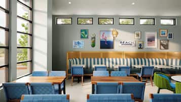 A beach-themed restaurant interior with a long bench seating area, individual tables, and framed artwork on the walls.