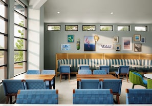 A beach-themed restaurant interior with a long bench seating area, individual tables, and framed artwork on the walls. - voco Solana Beach-Del Mar by IHG (Solana Beach)