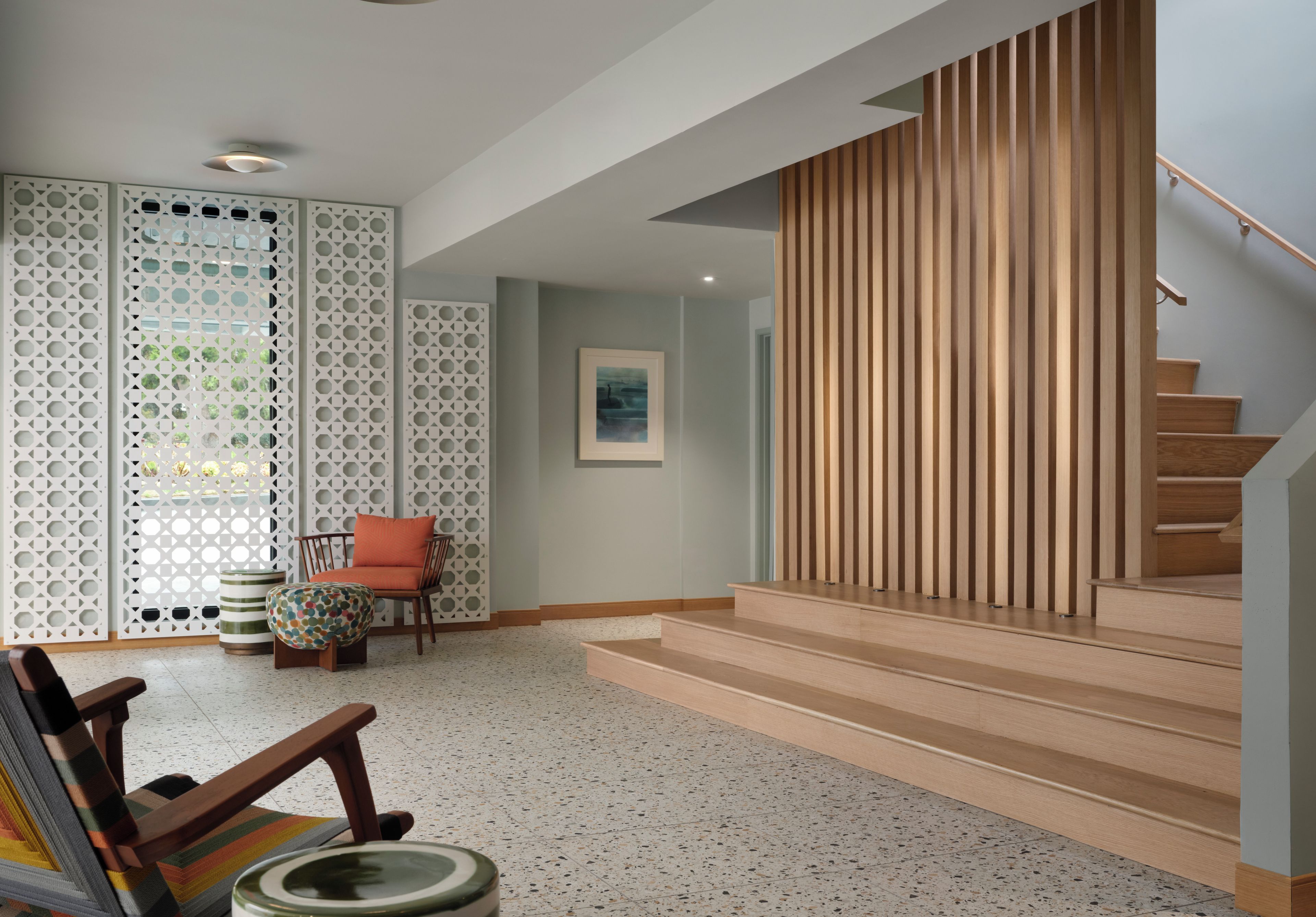 A modern interior with a staircase, a patterned wall, and a chair.