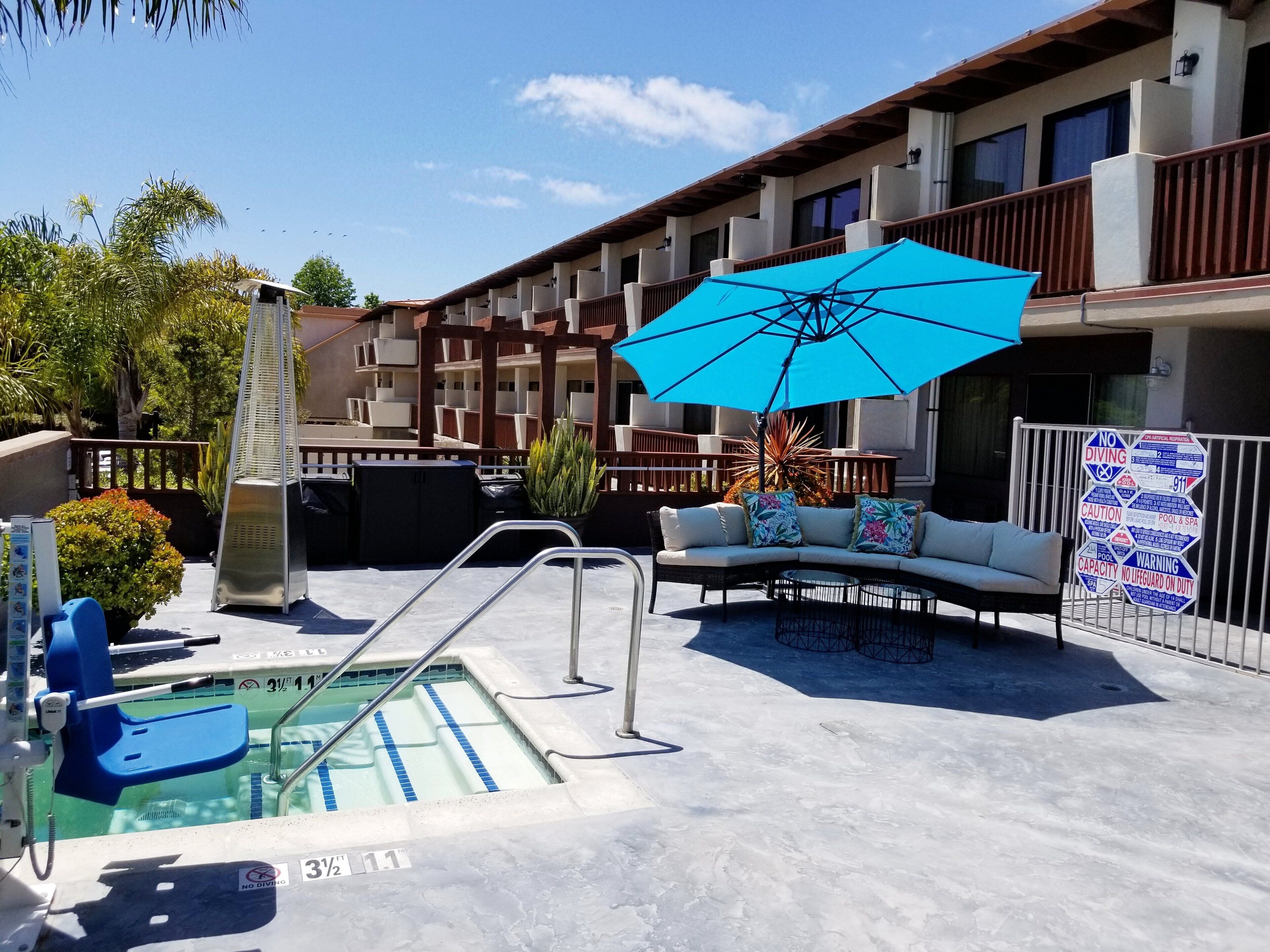 An outdoor pool area with a lounge chair, a blue umbrella, and a pool ladder.