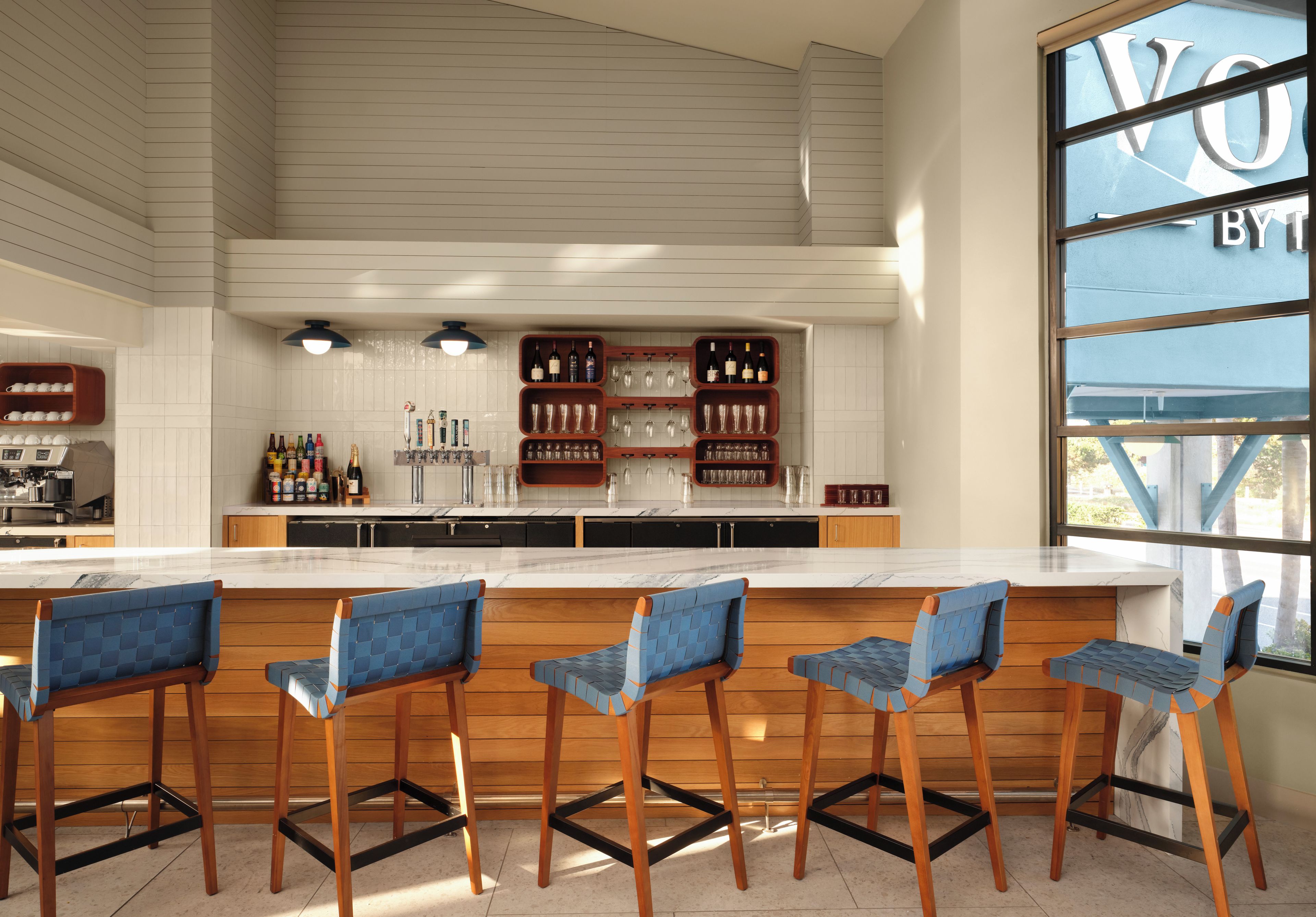 A modern kitchen with a bar area, wooden bar stools, and a large window.