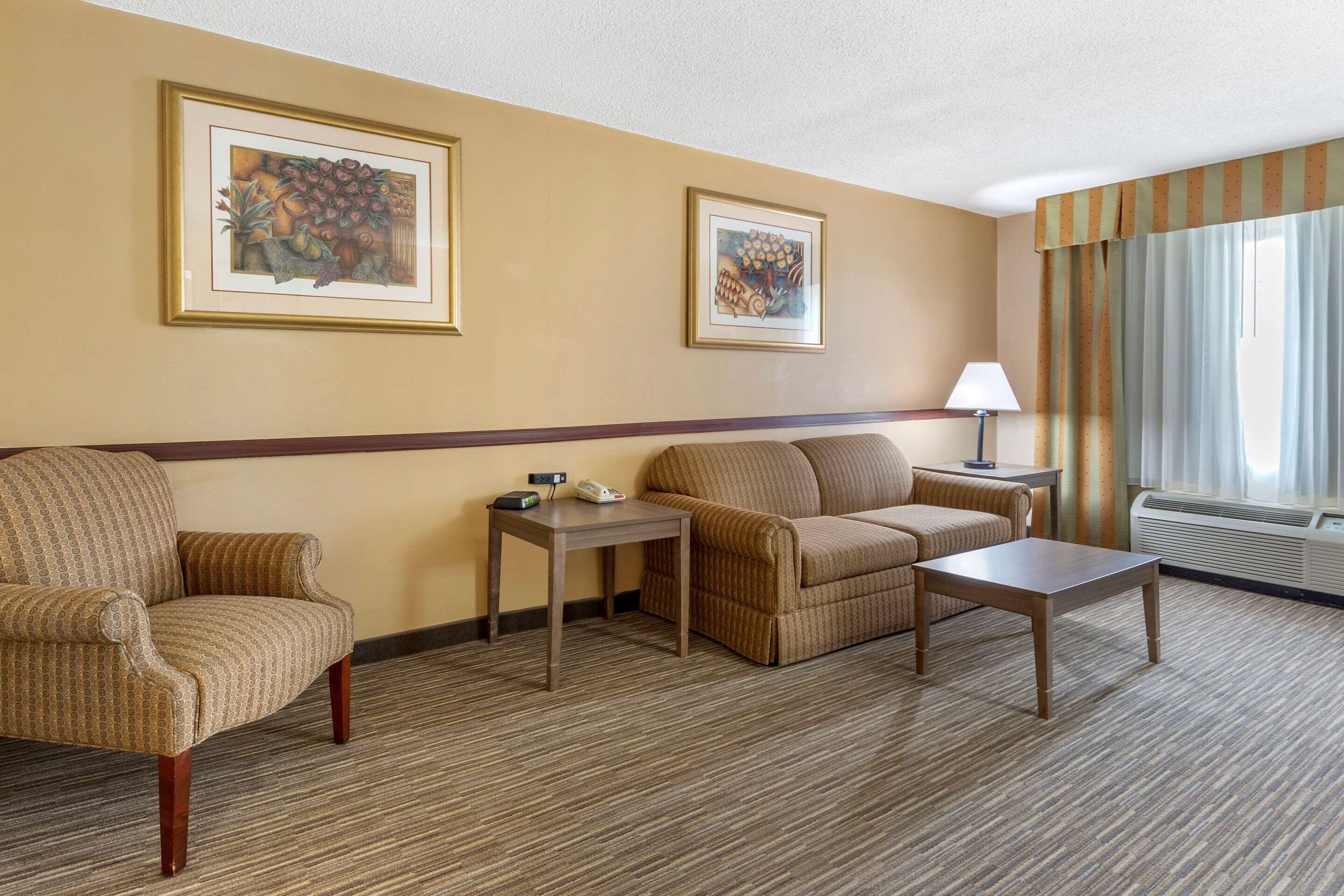 Habitación de hotel con sofá, sillón, dos mesas, una lámpara y cuadros en las paredes.