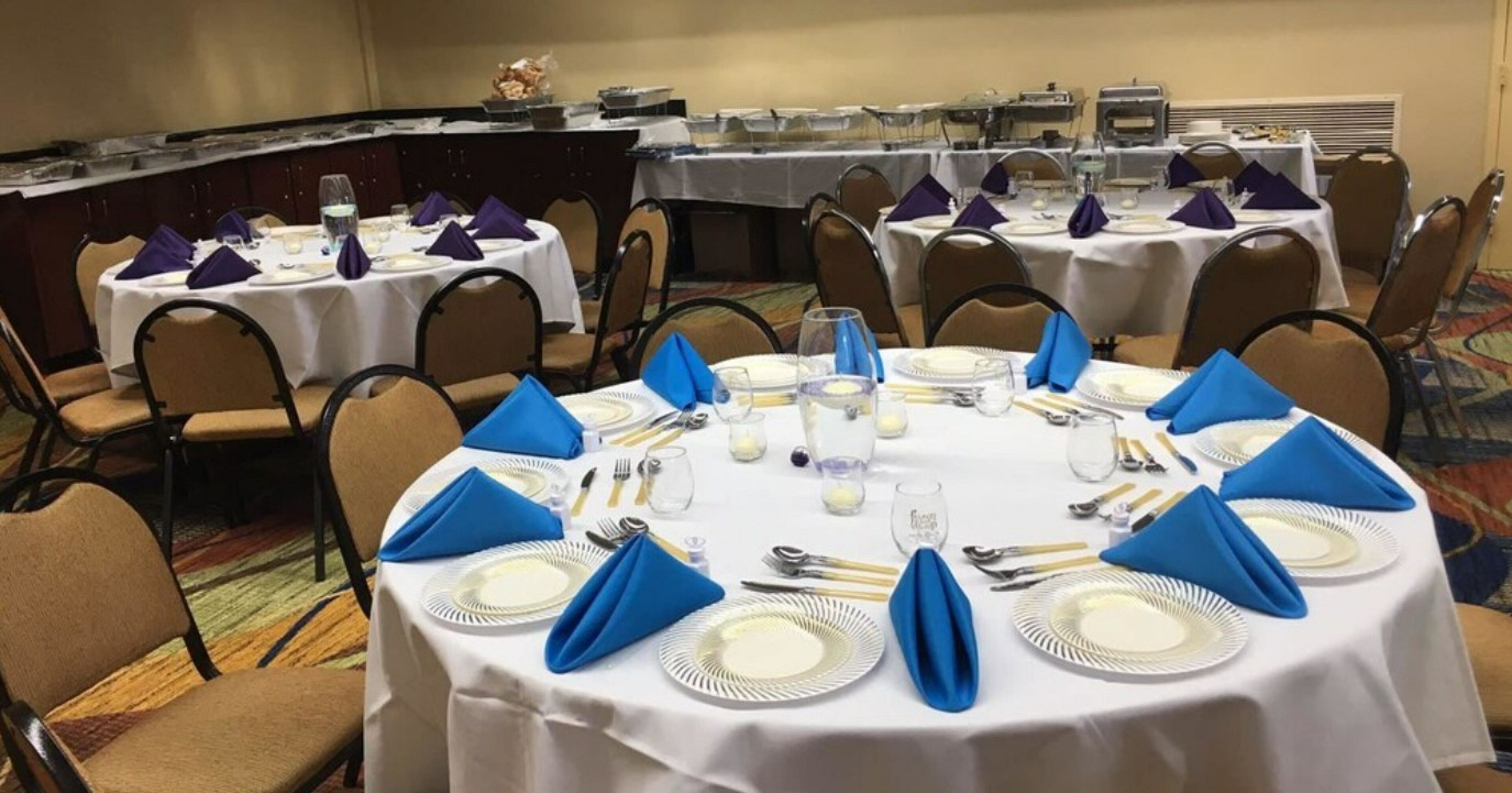 A conference room with round tables set for a meeting, each with white tablecloths, blue napkins, and silverware.