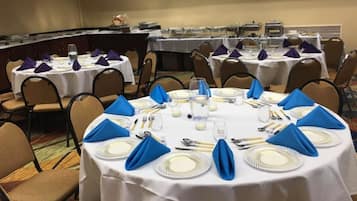 A conference room with round tables set for a meeting, each with white tablecloths, blue napkins, and silverware.