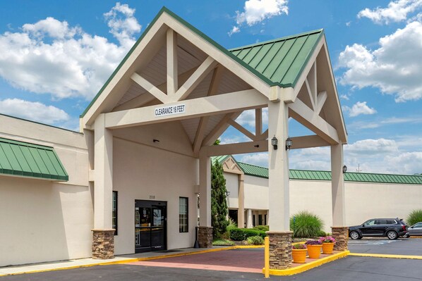 A hotel entrance with a covered area marked "Clearance 16 Feet" and a parking lot with cars. - Quality Inn & Suites Hanes Mall (Winston-Salem)