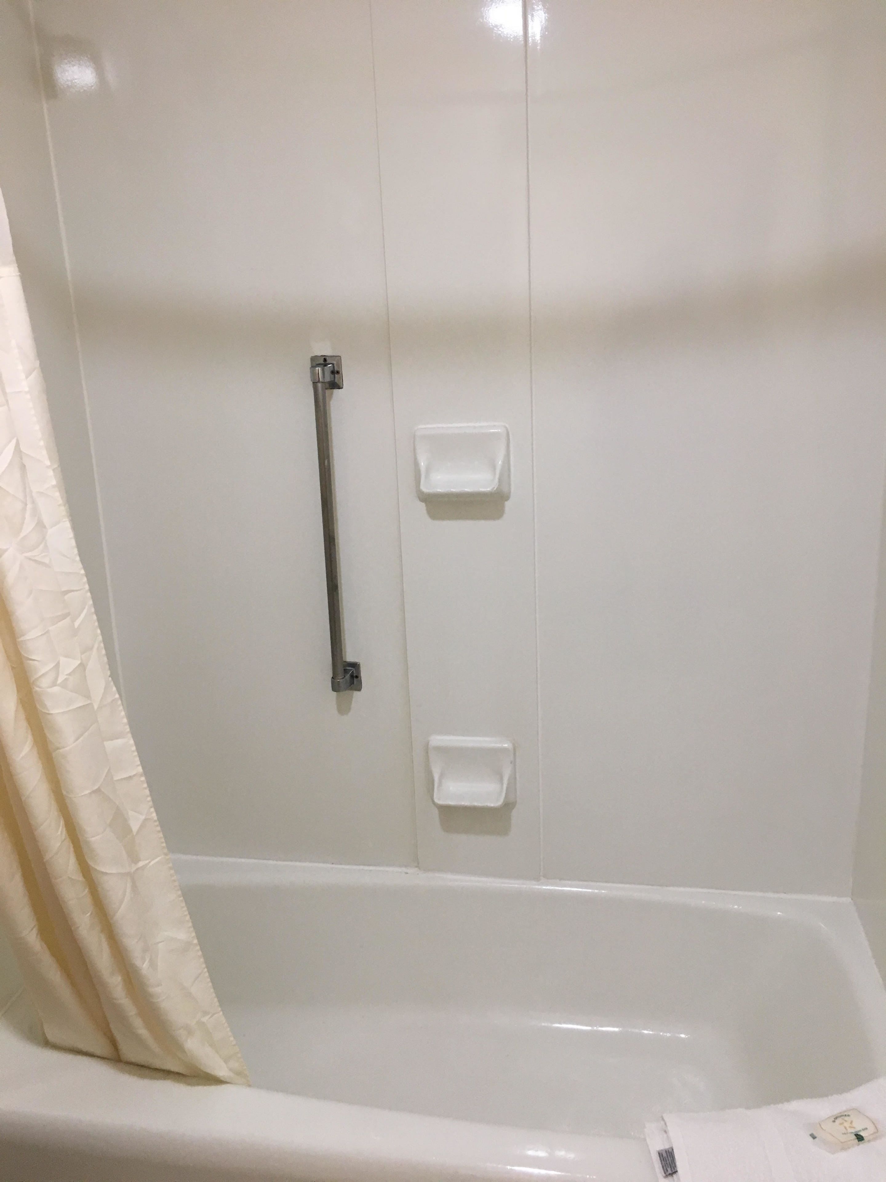 Une salle de bain avec une baignoire, un rideau de douche et deux porte-savons blancs fixés au mur.