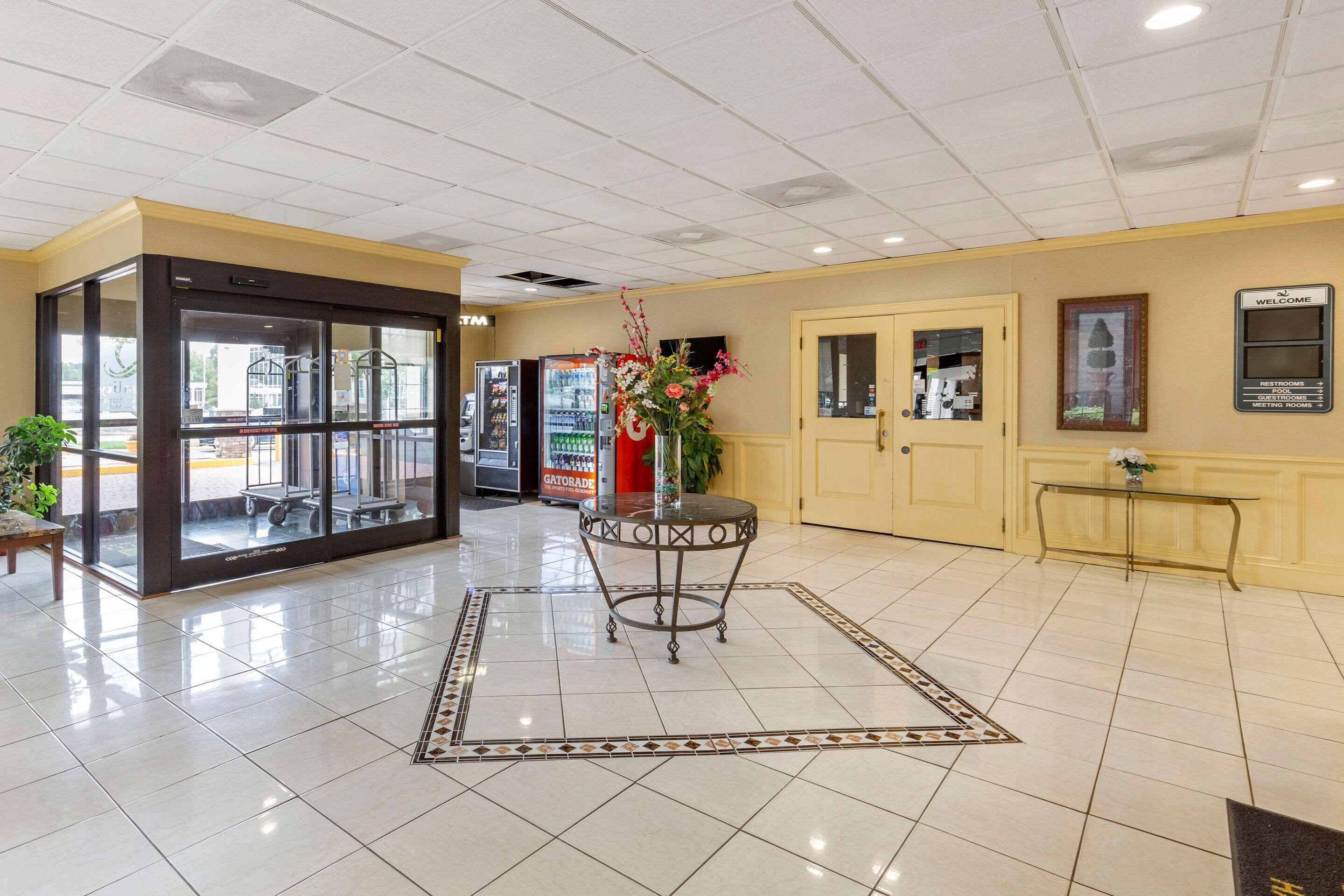 A hotel lobby with a tiled floor, a reception desk, a vending machine, and a glass door entrance.